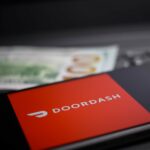 close up of mobile phone screen with logo lettering of Doordash payment provider on computer keyboard